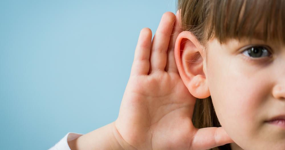 Child with hearing problem on blue background. Hearing loss in childhood, symptoms and treatment concept. Close up, copy space.